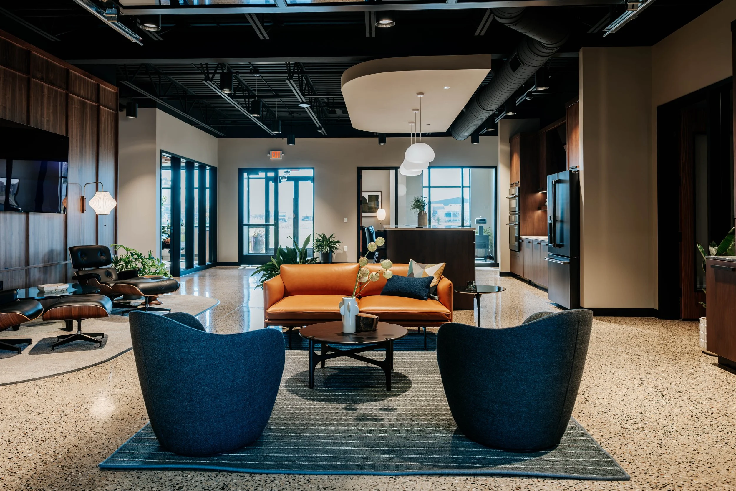 Office lounge at PDM Properties with an orange sofa, two blue chairs and polished concrete floors.
