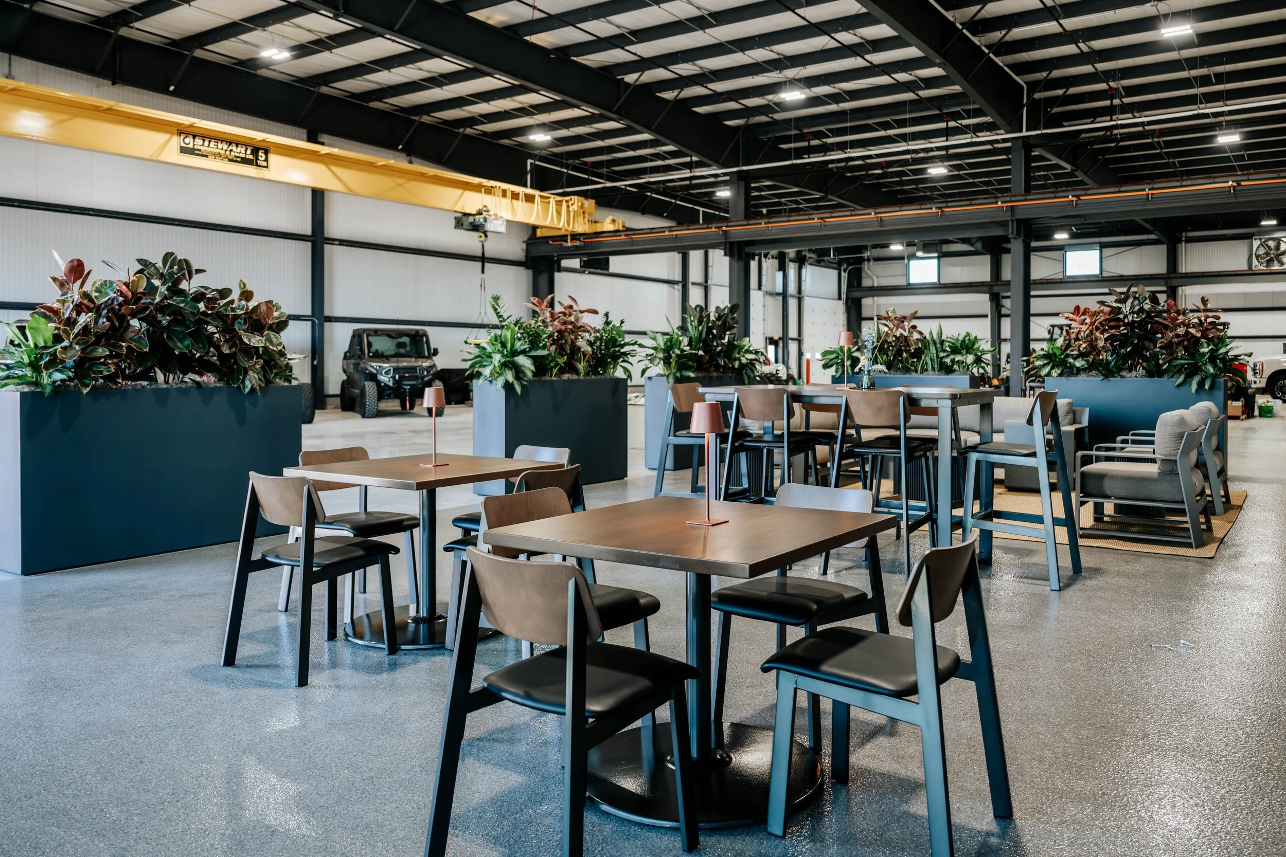 Dining tables and planters in the PDM Properties shop, with a yellow bridge crane overhead.