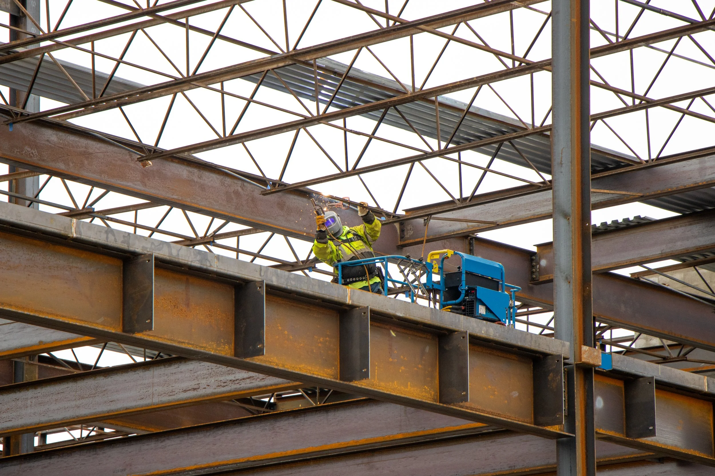Construction worker in yellow safety gear welding on a steel framework at a building site.