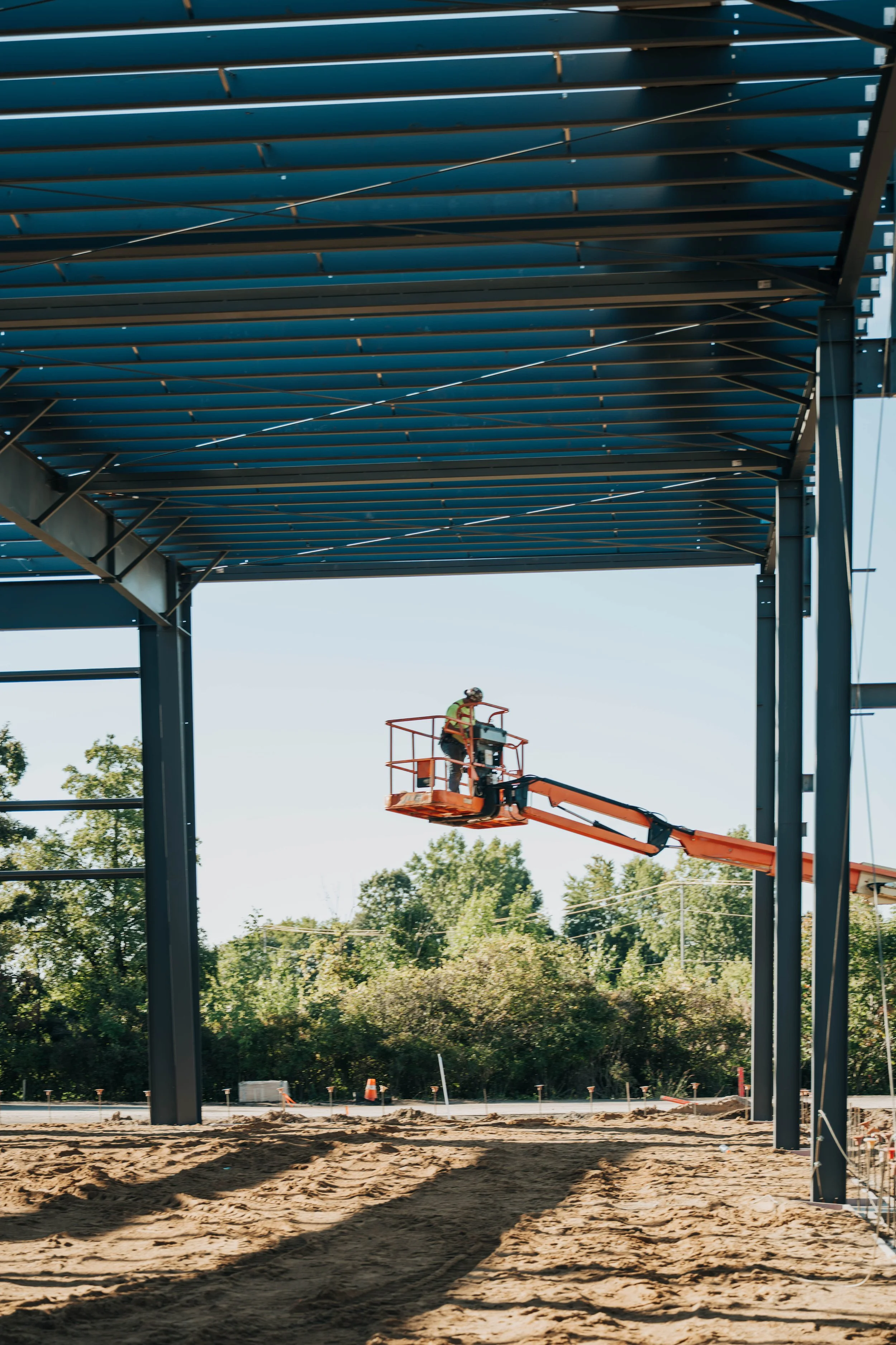 An FCC Construction crew member works from an orange boom lift beneath the roof steel of a building under construction at 5500 Broadmoor.