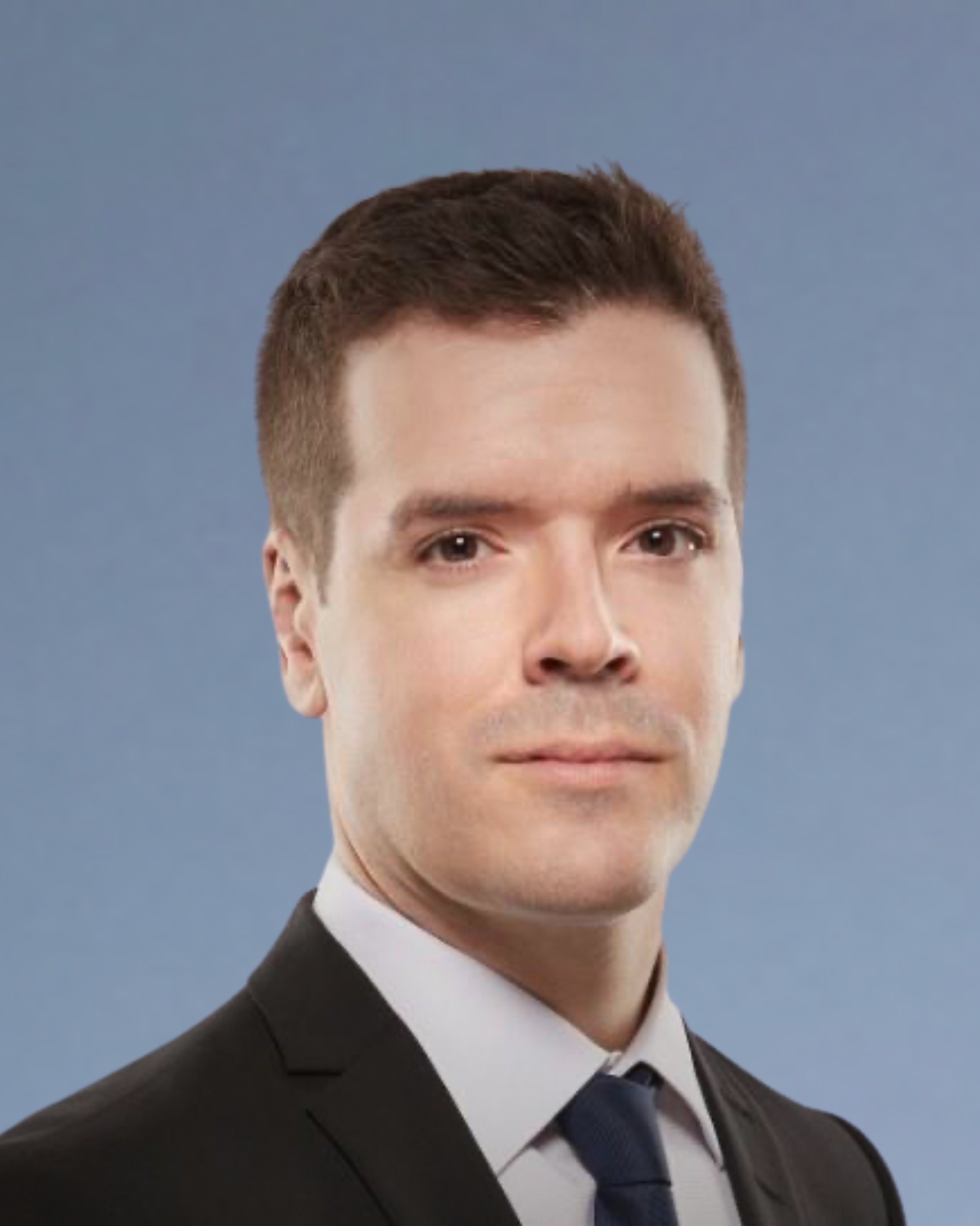 Professional portrait of a man with short dark hair in a suit and tie against a plain blue background.