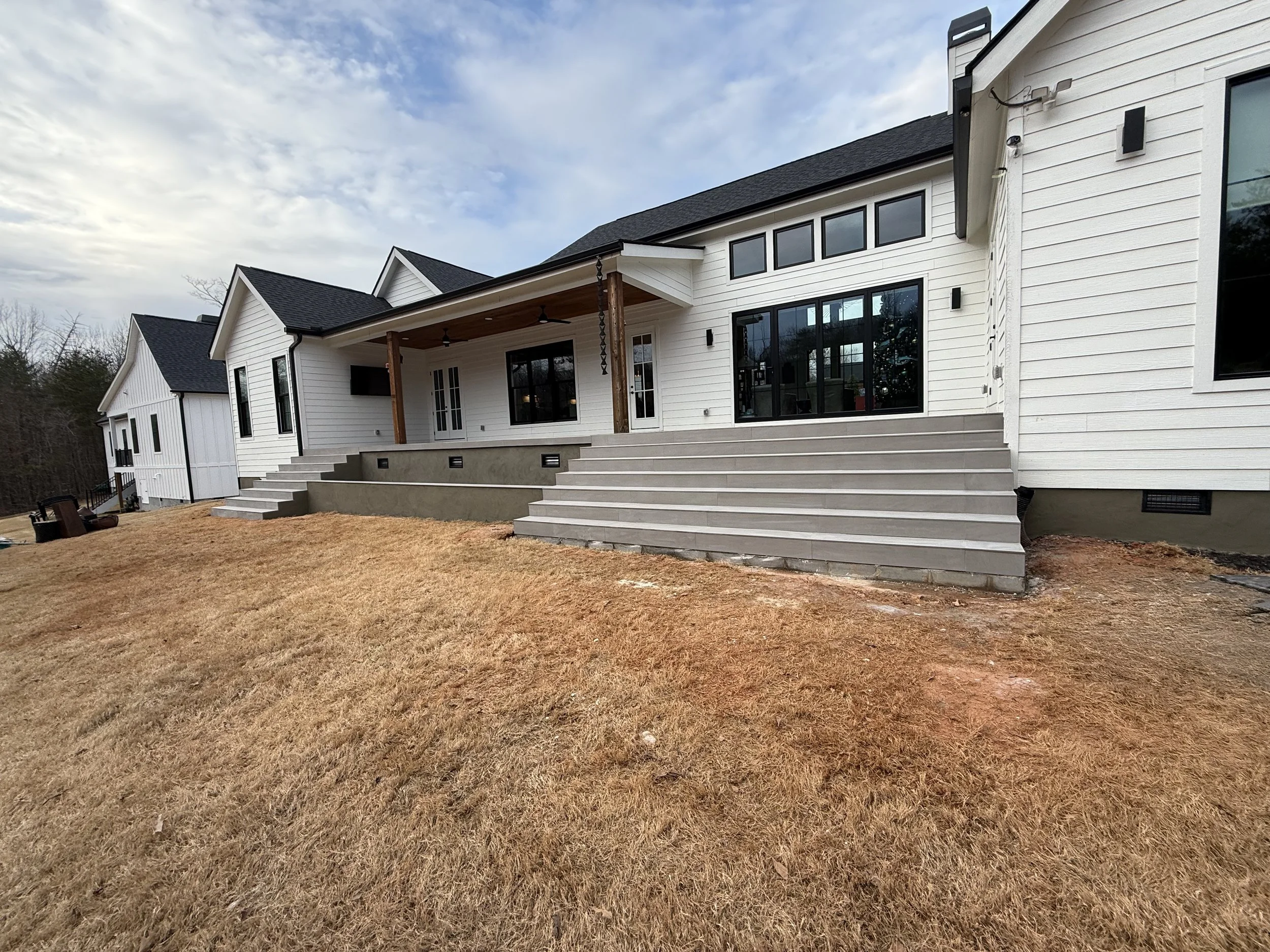 Newly constructed white house with multiple steps leading to a deck, black window frames, and a grassy yard.