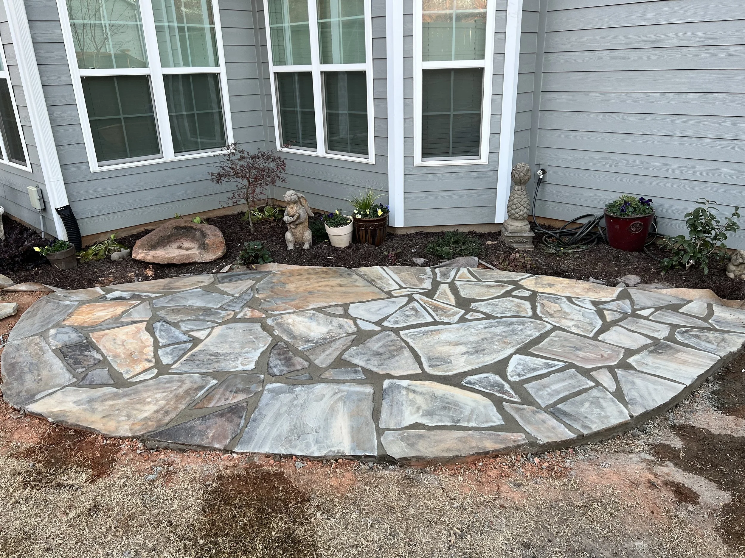 Finished stone patio in front of house with plants and garden statues.