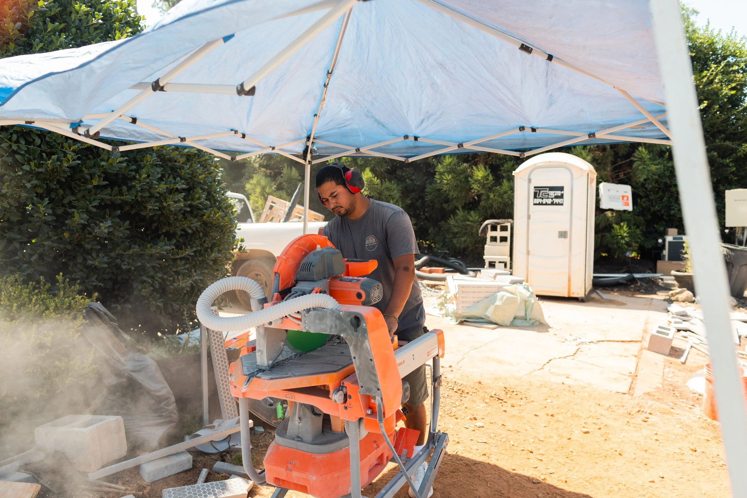 Man operating a concrete saw under a blue canopy at a construction site.