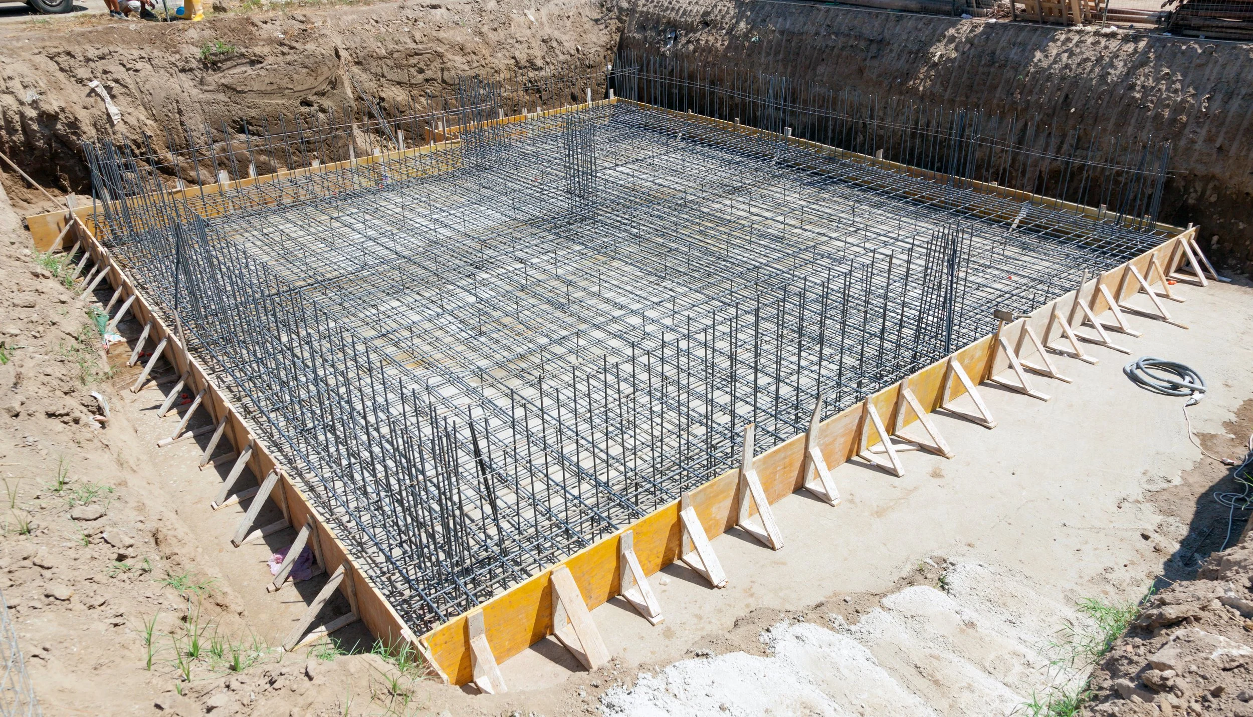 Construction site foundation with steel rebar reinforcement and wooden formwork for a concrete slab.