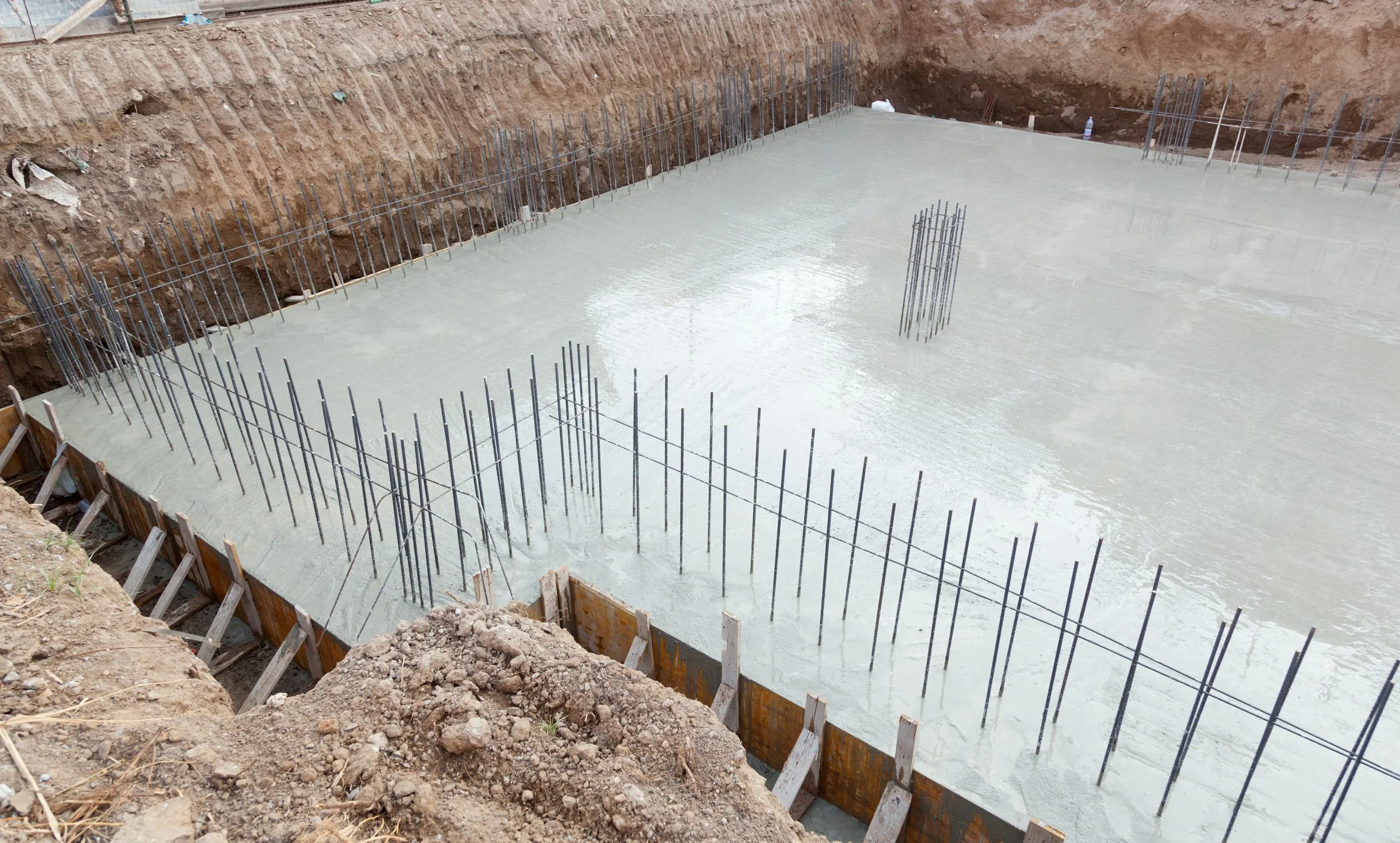 Concrete foundation being poured at a construction site, with rebar reinforcement protruding from the wet concrete.
