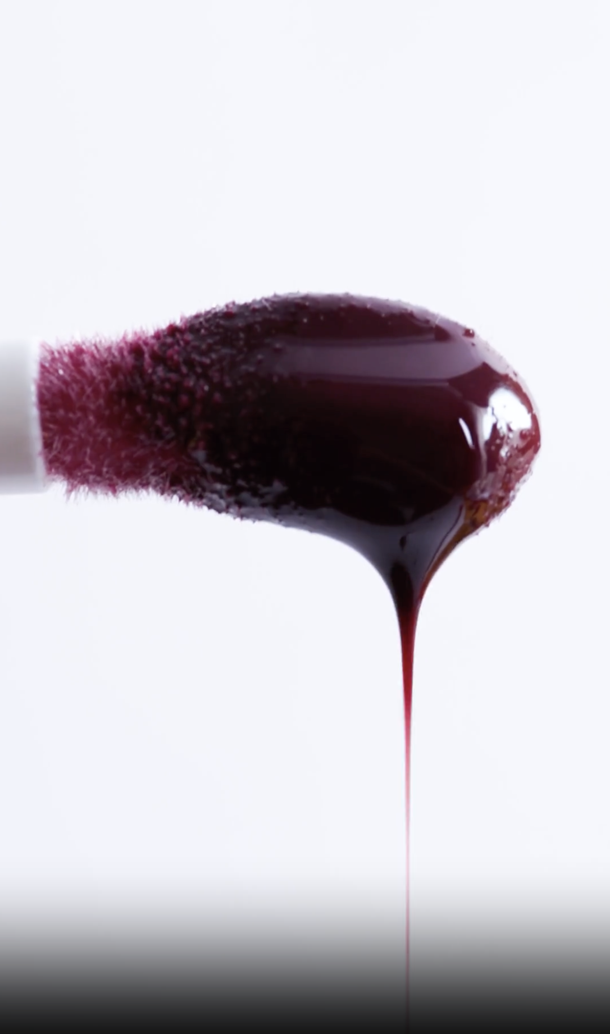Close-up of a lipstick applicator with dark red lipstick melting and dripping down, with a white background.