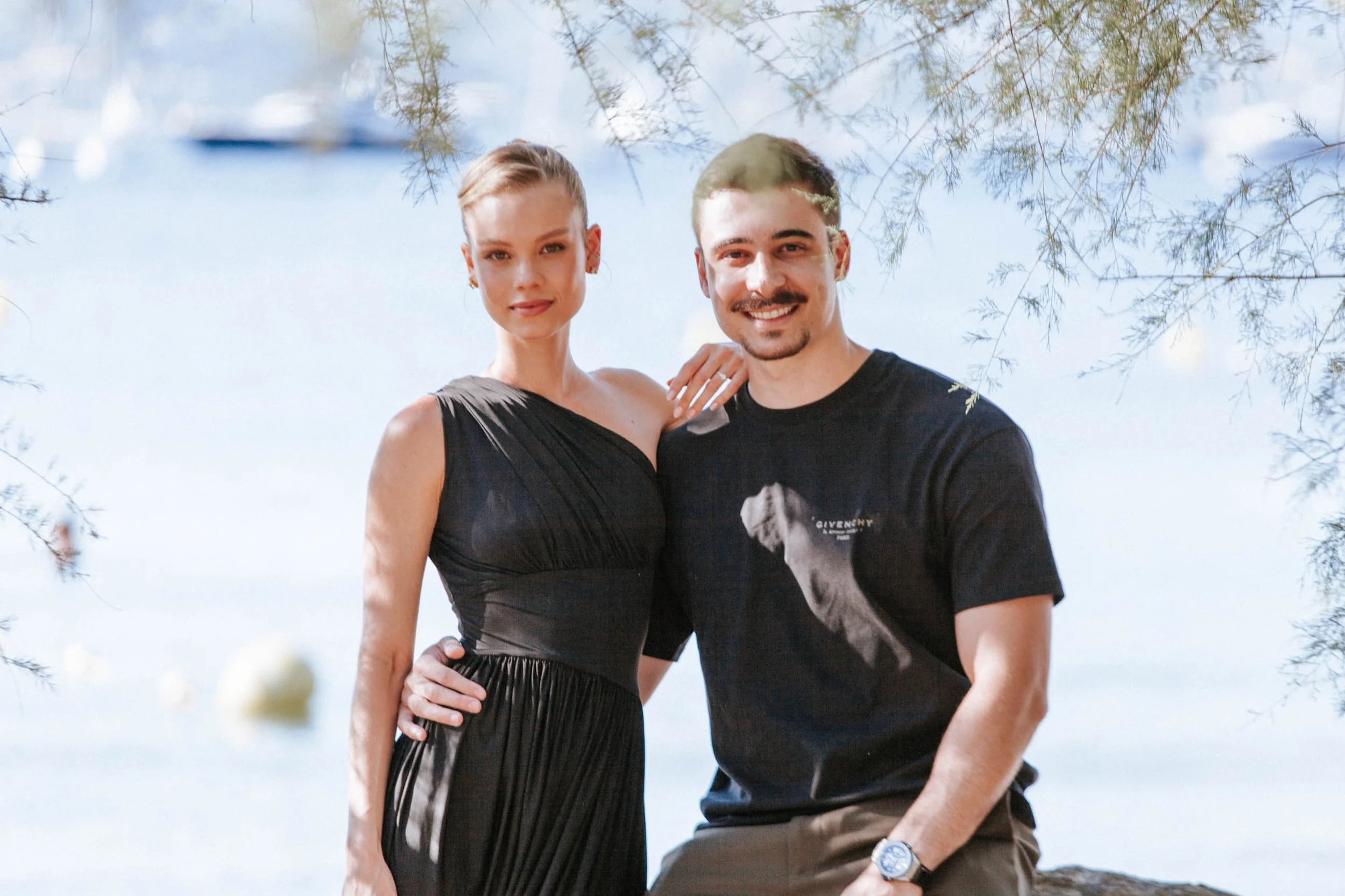 Séance photo de couple sous les tamaris au bord de l'eau, baie et bateaux au mouillage en arrière-plan, Golfe de Saint-Tropez