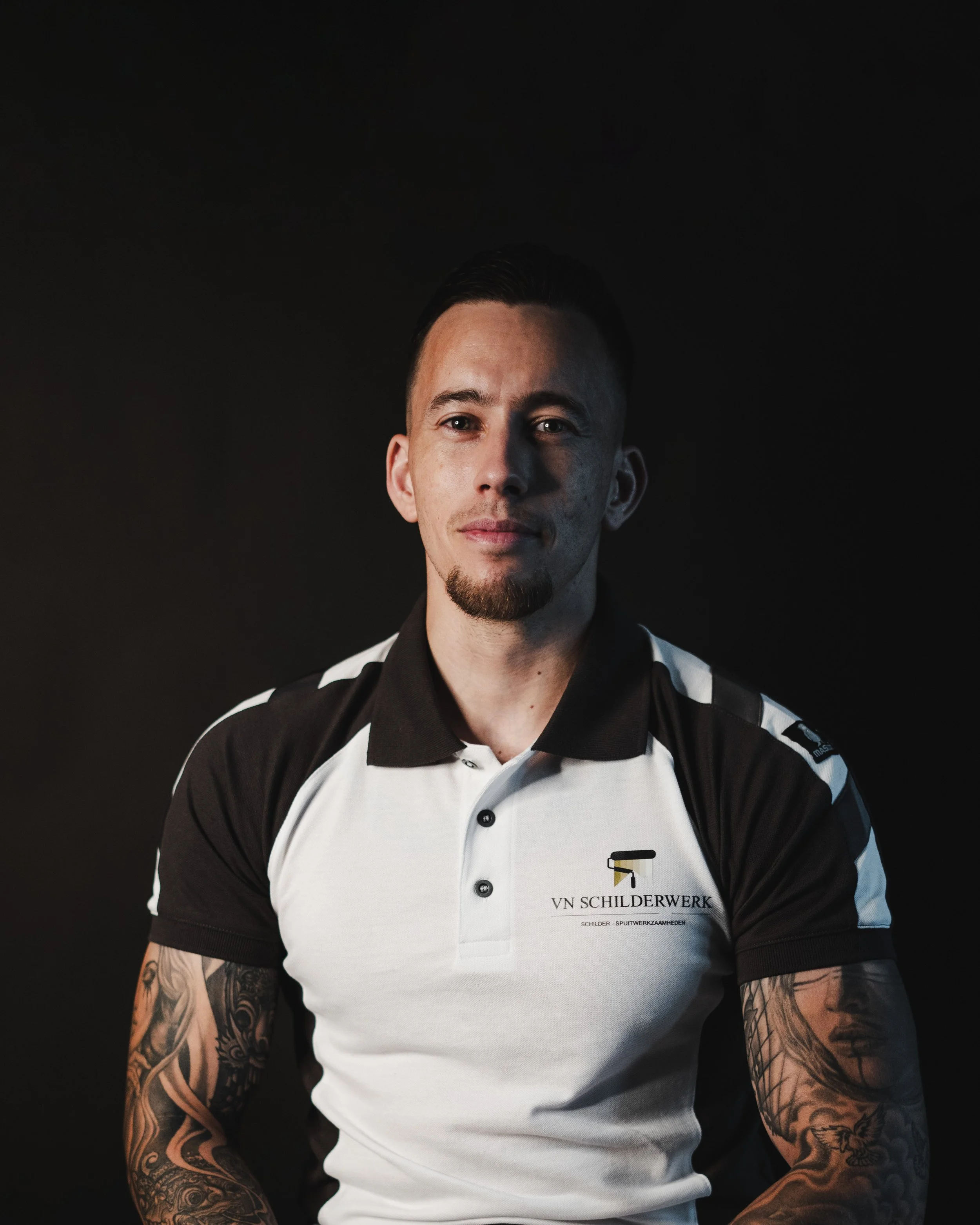 Portret van een man zwarte en witte schilderoutfit, achtergrond donker, glimlachend.