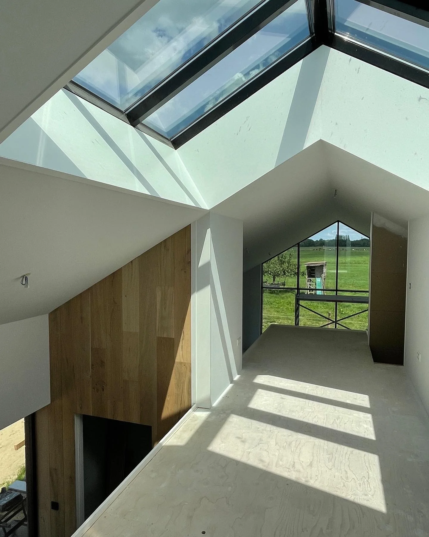 Interieur van een nieuwbouwhuis met grote dakramen, veel natuurlijk licht en uitzicht op groene velden.