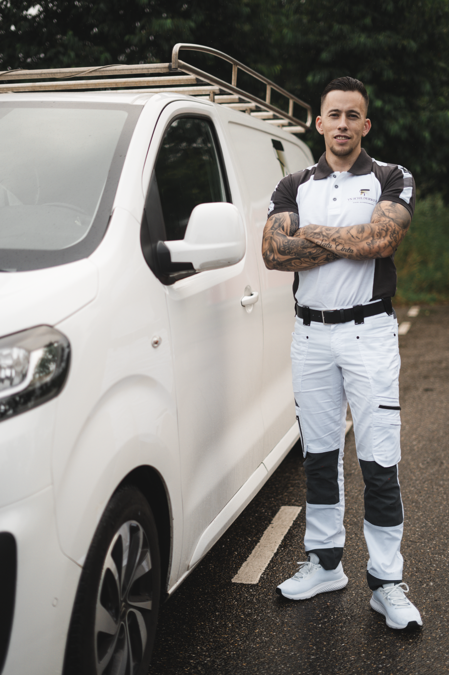 Man is schilder en staat naast een witte bedrijfswagen met een ladder op het dak.