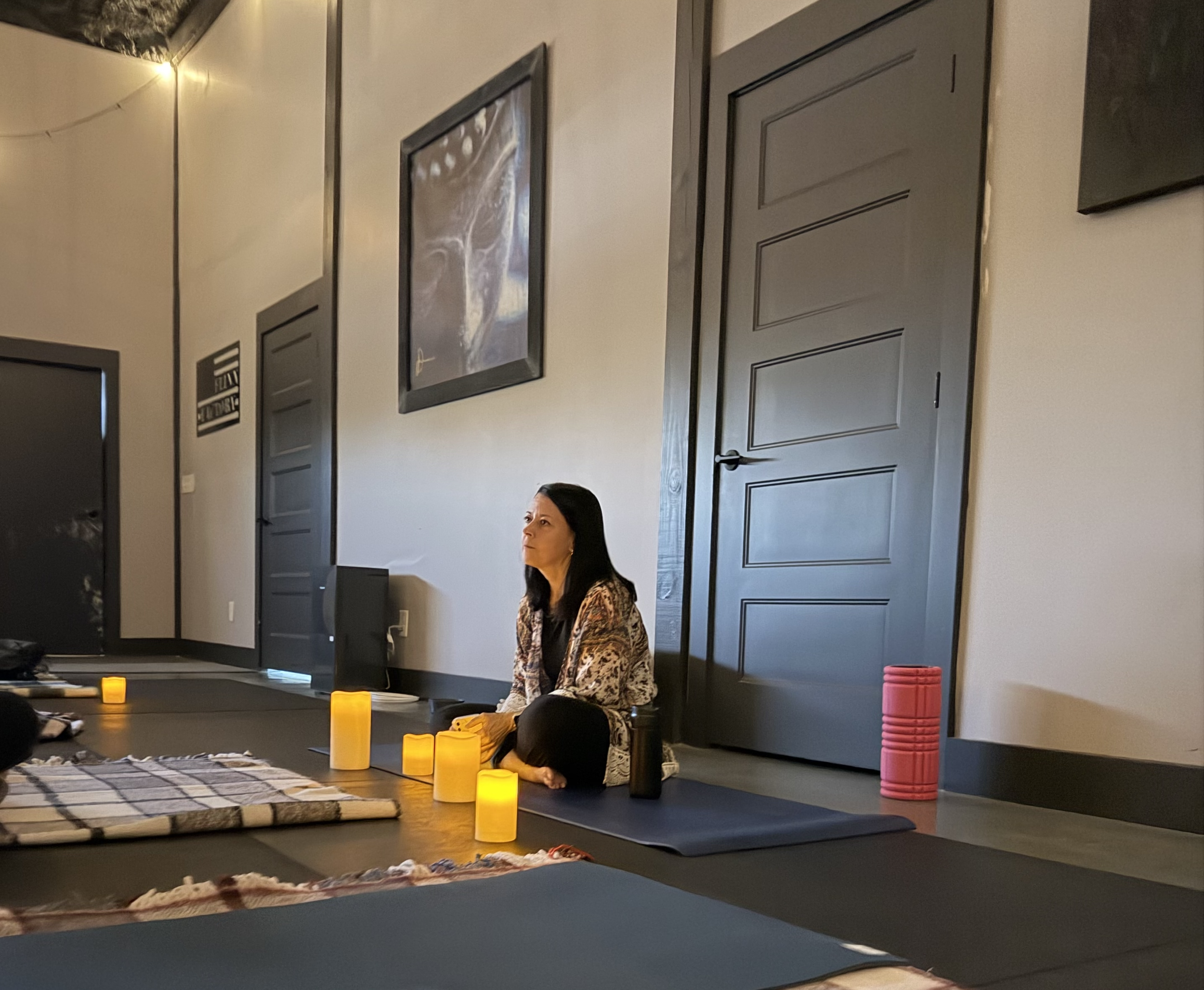 Woman sitting peacefully in a softly lit room surrounded by candles and yoga mats during a somatic breathwork session, symbolizing quiet confidence and inner stillness.