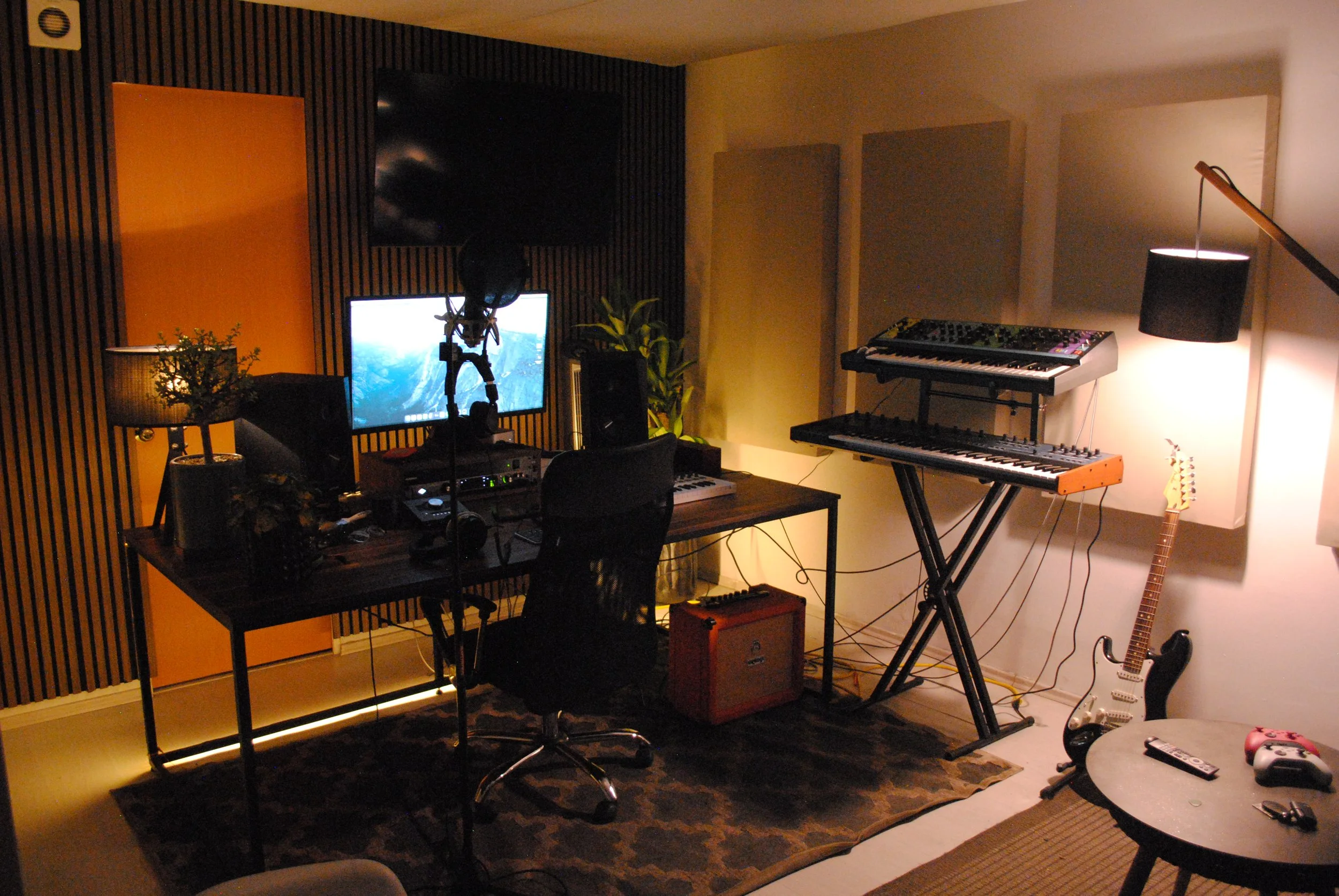 Estudio de grabación casero con computador, micrófono, teclado, guitarra eléctrica y consola de sonido.