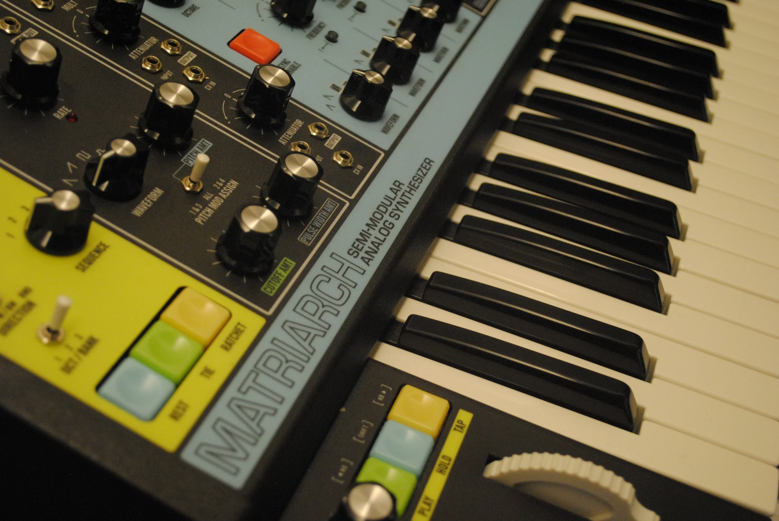 Un teclado de sintetizador musical con knobs y botones, con la marca 'MOOG', y palancas de control de volumen y cambios en la parte inferior izquierda.