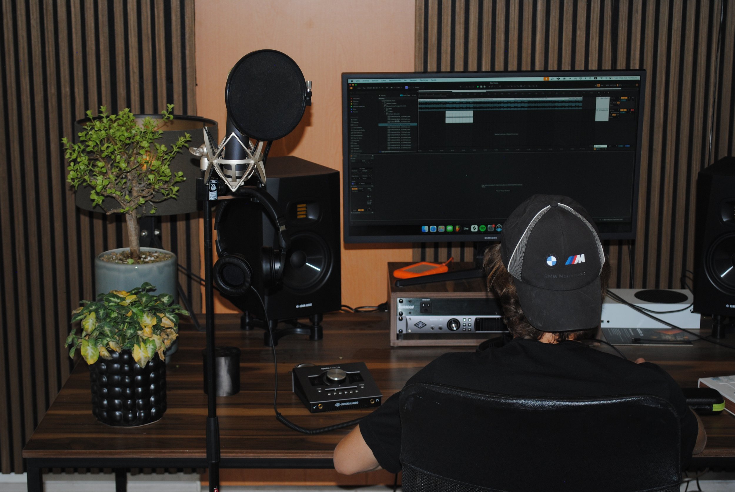 Estudio de grabación con computadora, monitoreo de audio, plantas en macetas y micrófono en soporte