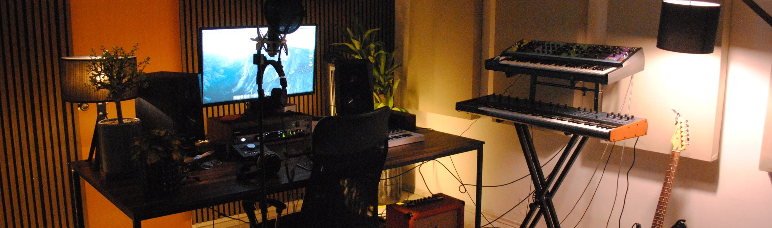 Estudio de música con teclado, computadora y equipo de grabación en un ambiente acogedor con plantas y lámparas.