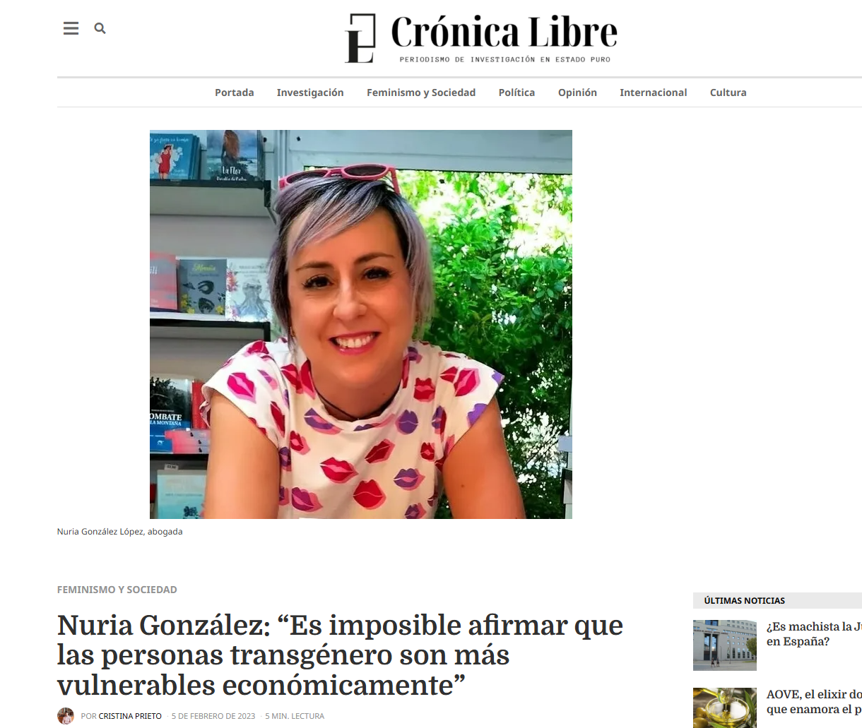 Foto de una mujer sonriendo, con cabello rubio y vestido con estampado de labios en color rosa y morado, en una librería con libros en el fondo.
