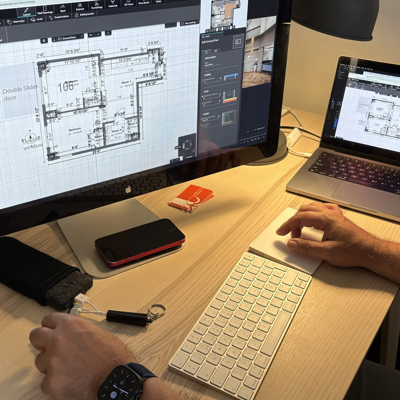 Craig, working on architectural floor plan designs at a desk, with a smartphone, a keychain, and a small notebook nearby.