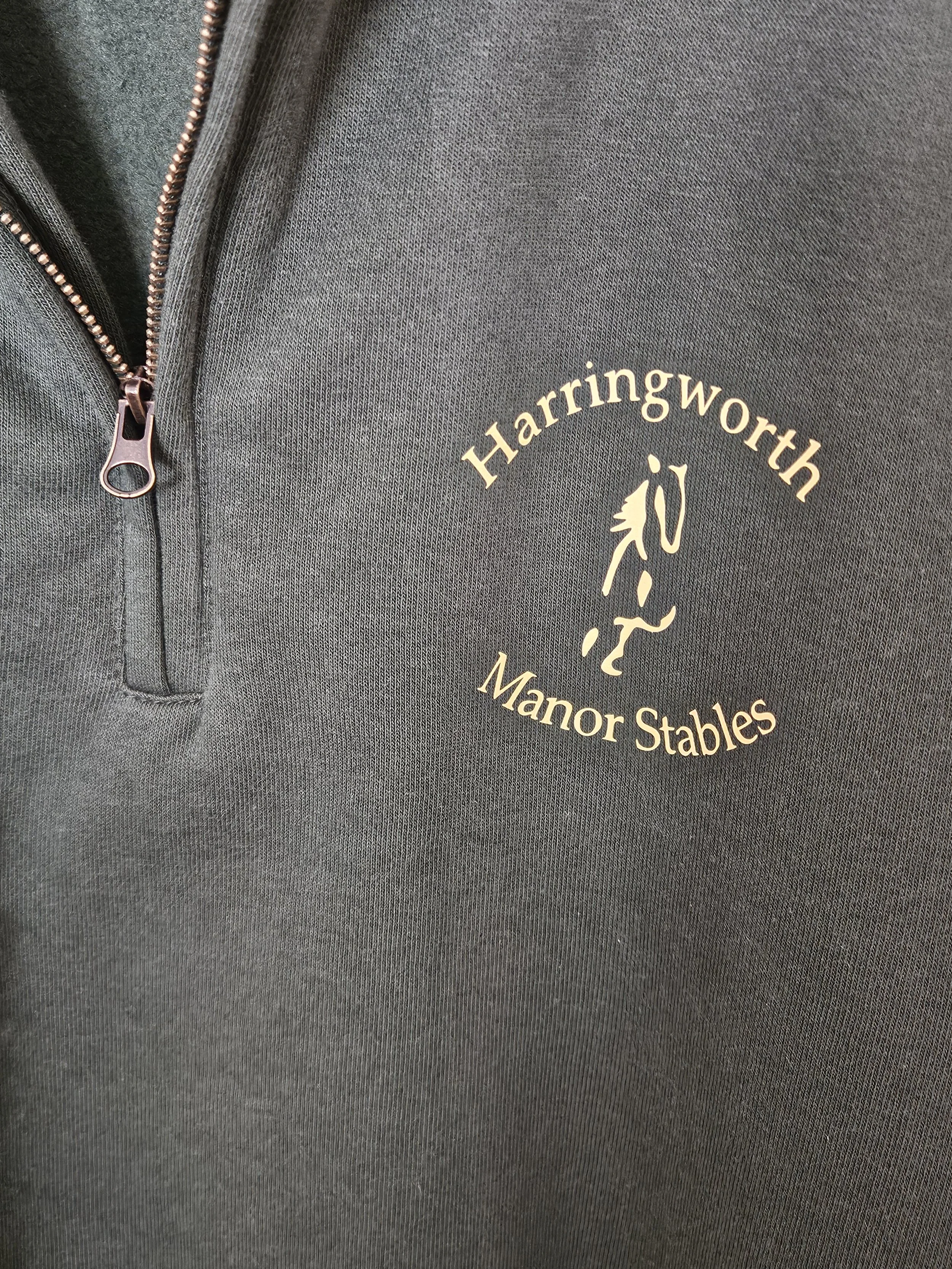 A gray fabric garment with a zippered pocket on the left and a logo reading 'Harringworth Manor Stables' along with a horse head emblem.