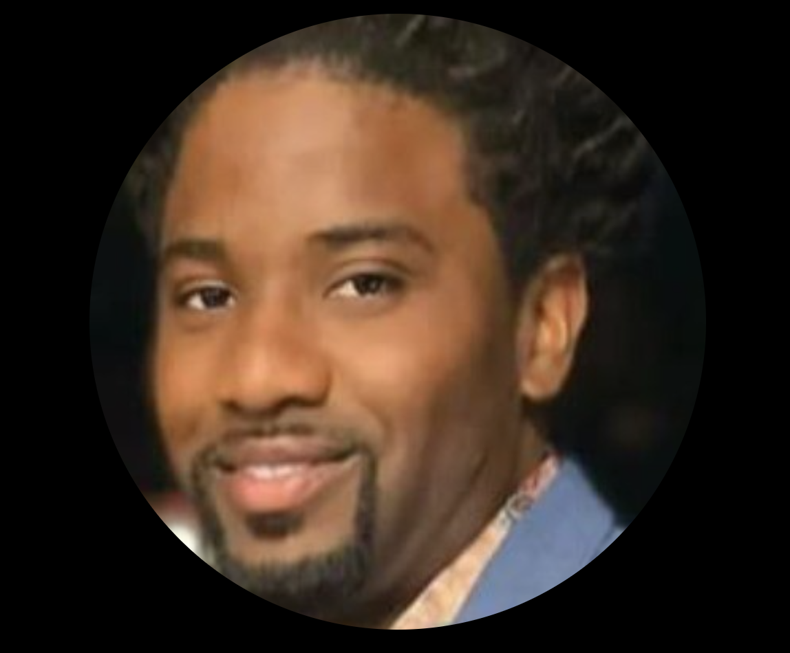 Close-up of a smiling person with short, curly hair and a goatee.