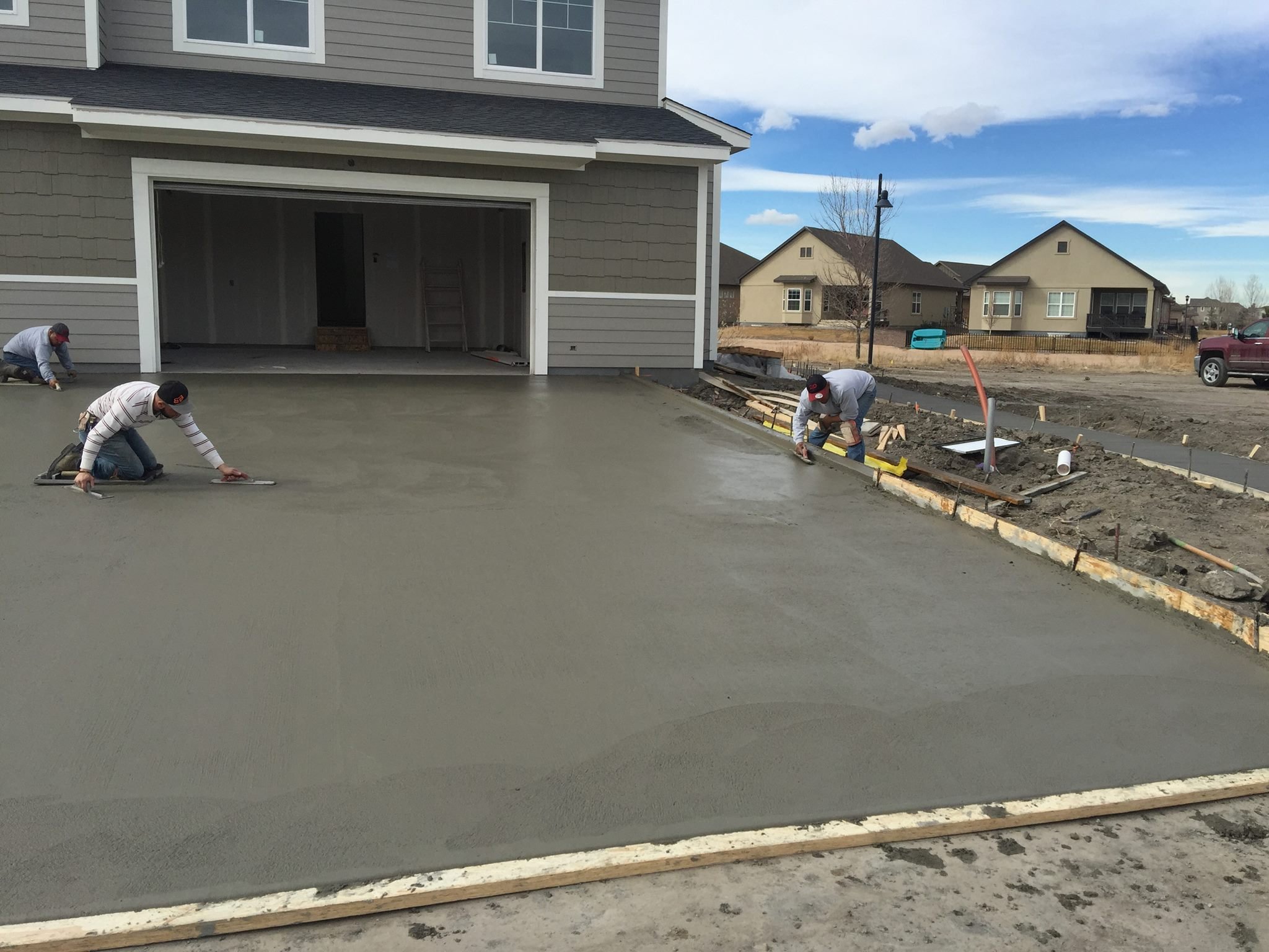 Workers leveling freshly poured concrete for a driveway in front of a house.