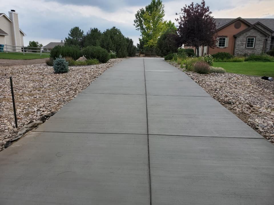 Concrete driveway with adjacent rock landscaping and trees in a residential area.