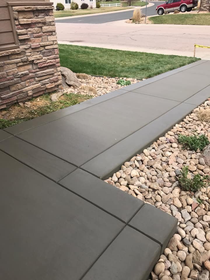 Freshly laid concrete sidewalk with decorative stone edging and red SUV on a suburban street.