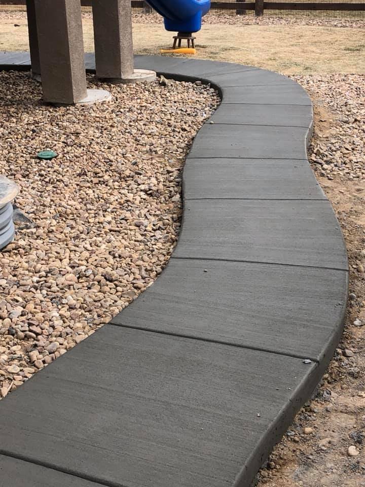 Curved concrete walkway bordered by gravel in a landscaped area with a playground in the background.