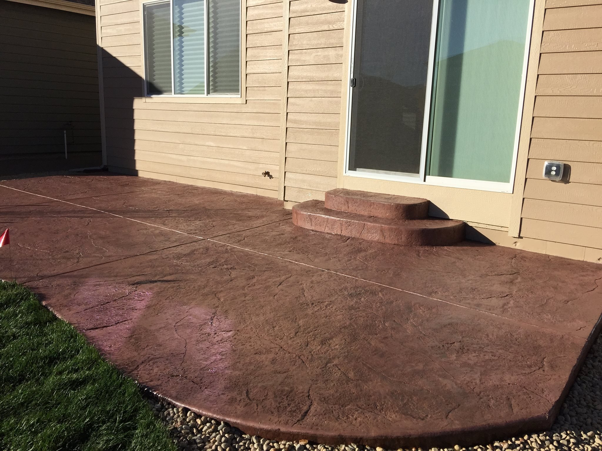 Concrete patio with steps leading to a sliding glass door on a house.