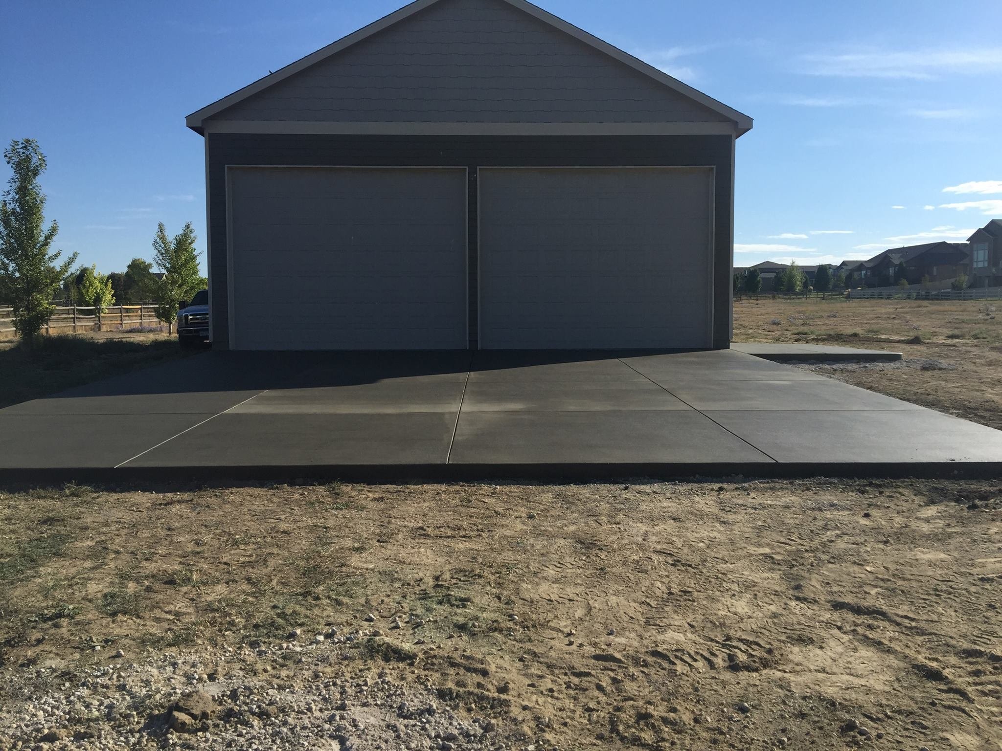 A newly poured concrete driveway leading to a two-door garage in a residential area.