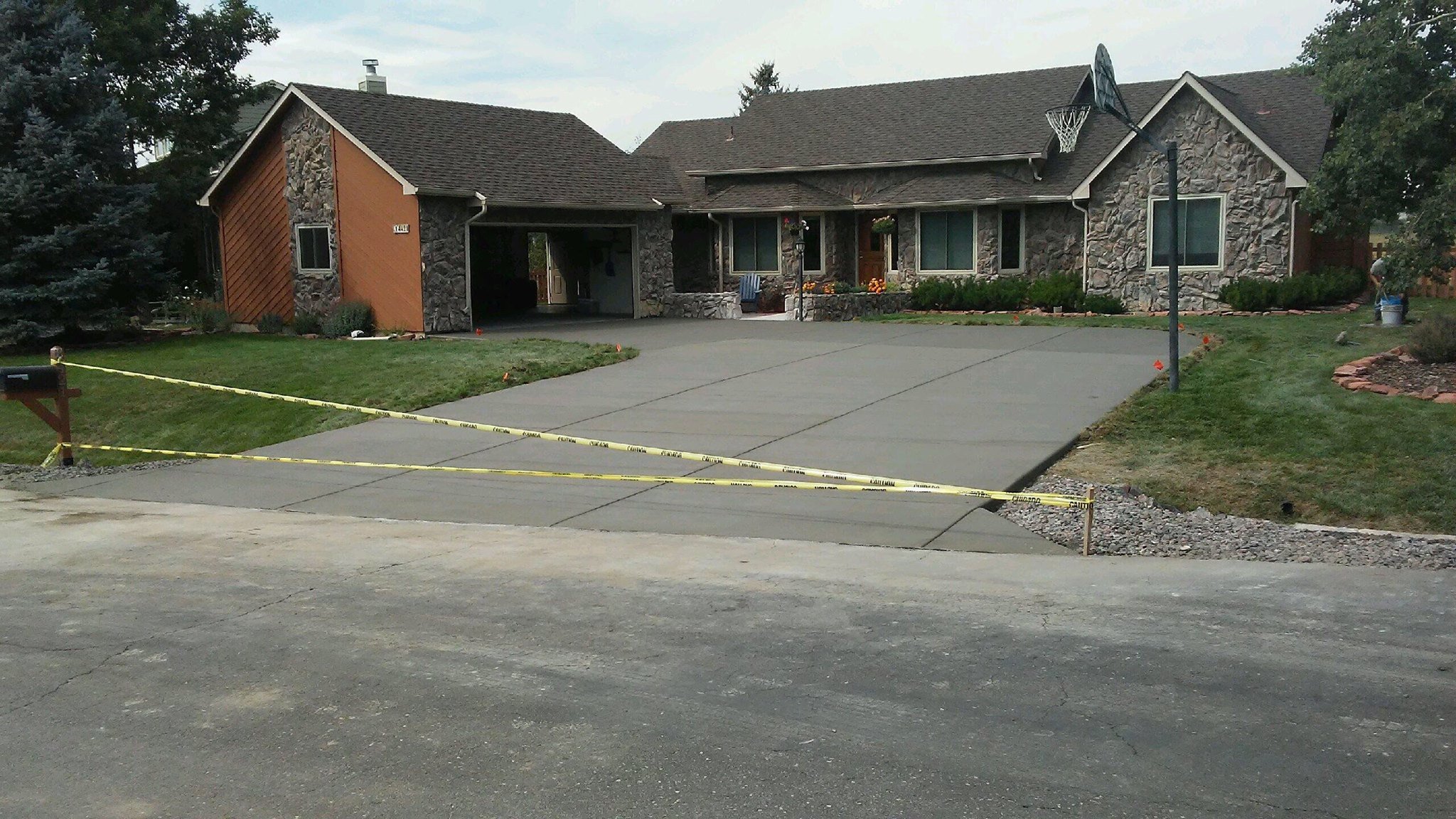 Residential home with a new concrete driveway, caution tape around driveway, stone exterior, and basketball hoop.