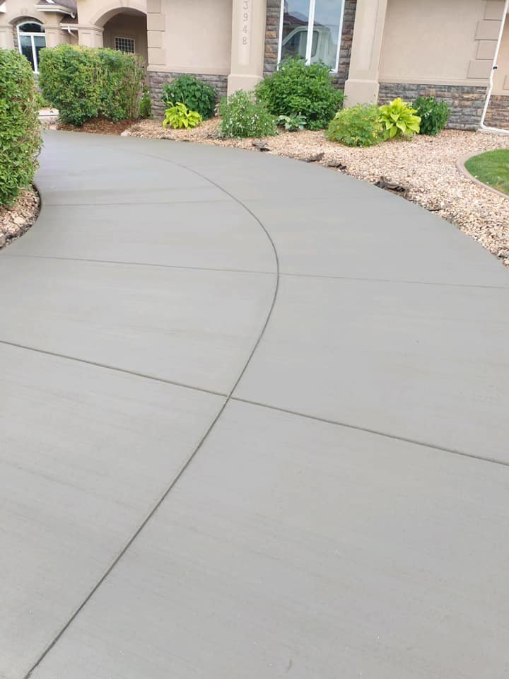 Freshly poured concrete walkway leading to house entrance with trimmed shrubs and rock landscaping.
