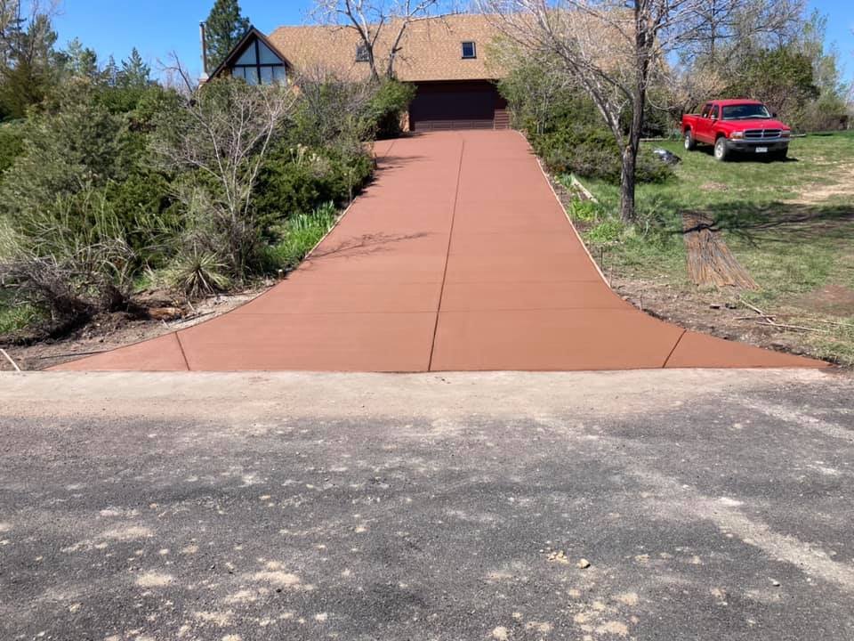 Newly poured concrete driveway leading to a house with a garage, surrounded by trees and a red truck parked on the side.