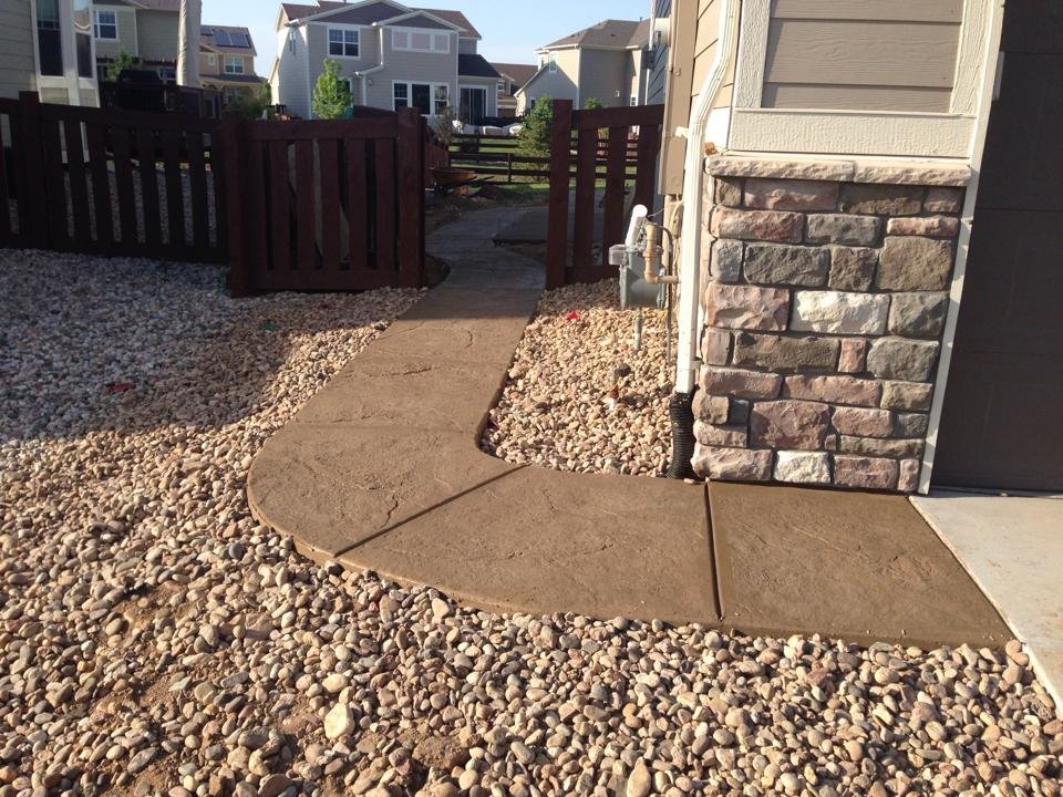 Stone pathway through a rocky yard leading to a wooden gate and houses in the background.