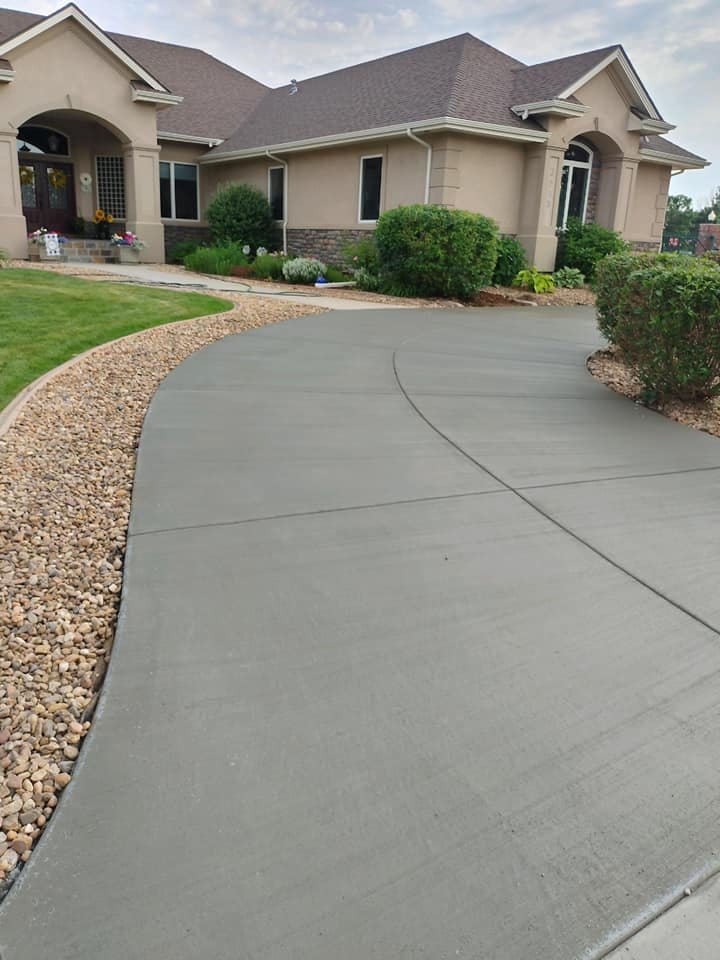 House exterior with a new concrete driveway, landscaped with green shrubs and pebbled edging, leading to the front entrance.
