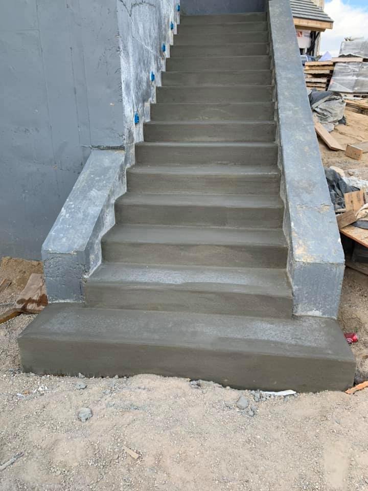 Newly constructed concrete stairs at a building site, with surrounding materials and unfinished surfaces visible.