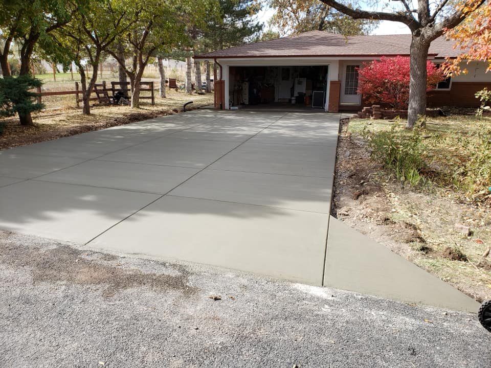 Freshly paved concrete driveway leading to a house surrounded by trees and bushes.