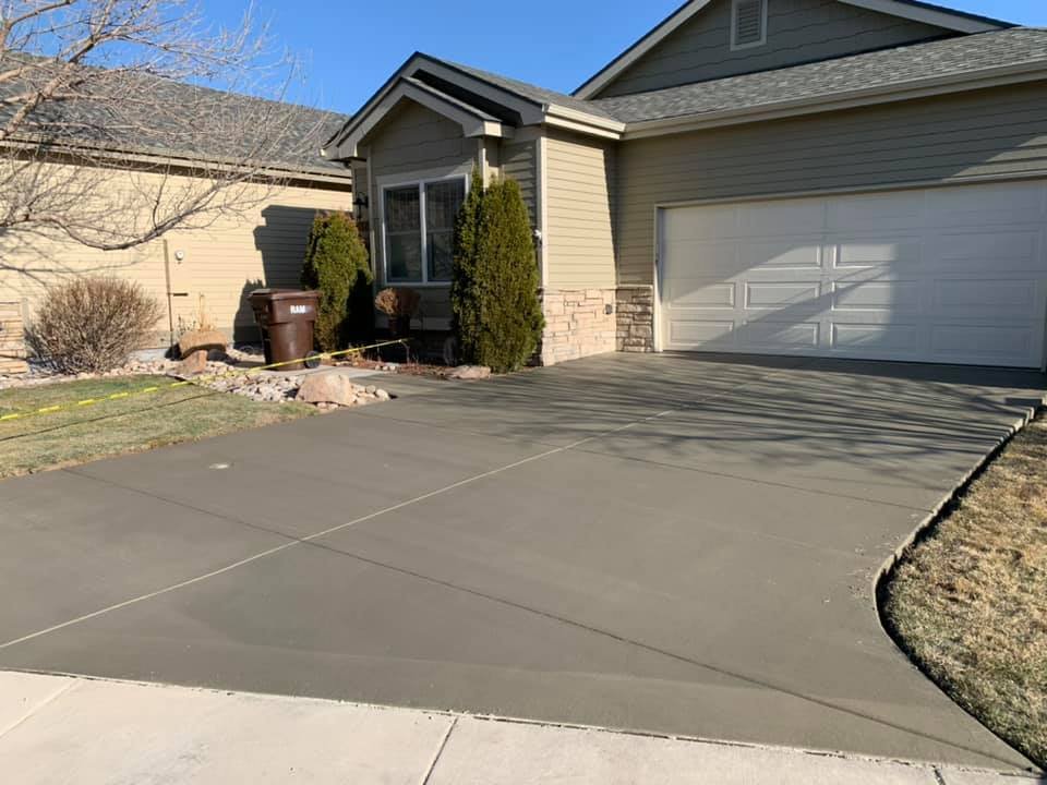 House with freshly paved concrete driveway and garage door, surrounded by a small garden and shrubs.