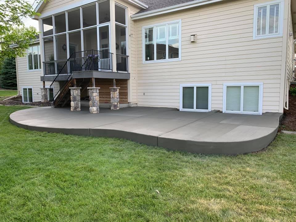 A backyard view of a beige house with a screened porch, stone pillars, and a curved concrete patio.
