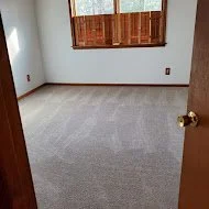 Empty room with beige carpet, tan walls, and a window with closed wooden blinds, viewed from an open doorway.
