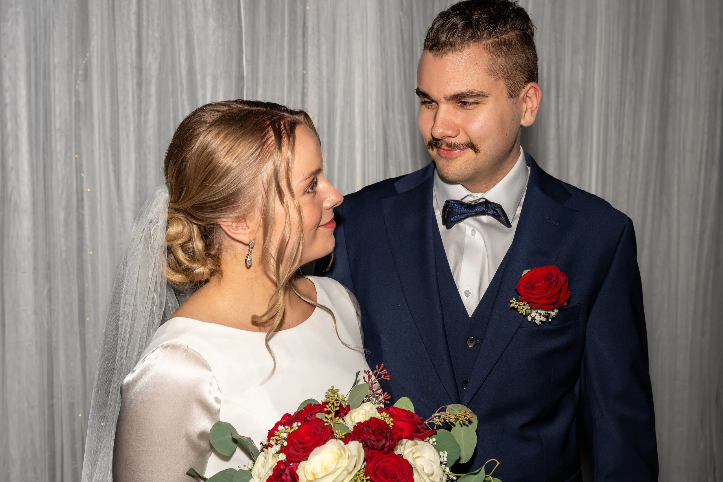 Hääpari katsoo hellästi toisiaan, morsiammella kukkakimppu kädessä