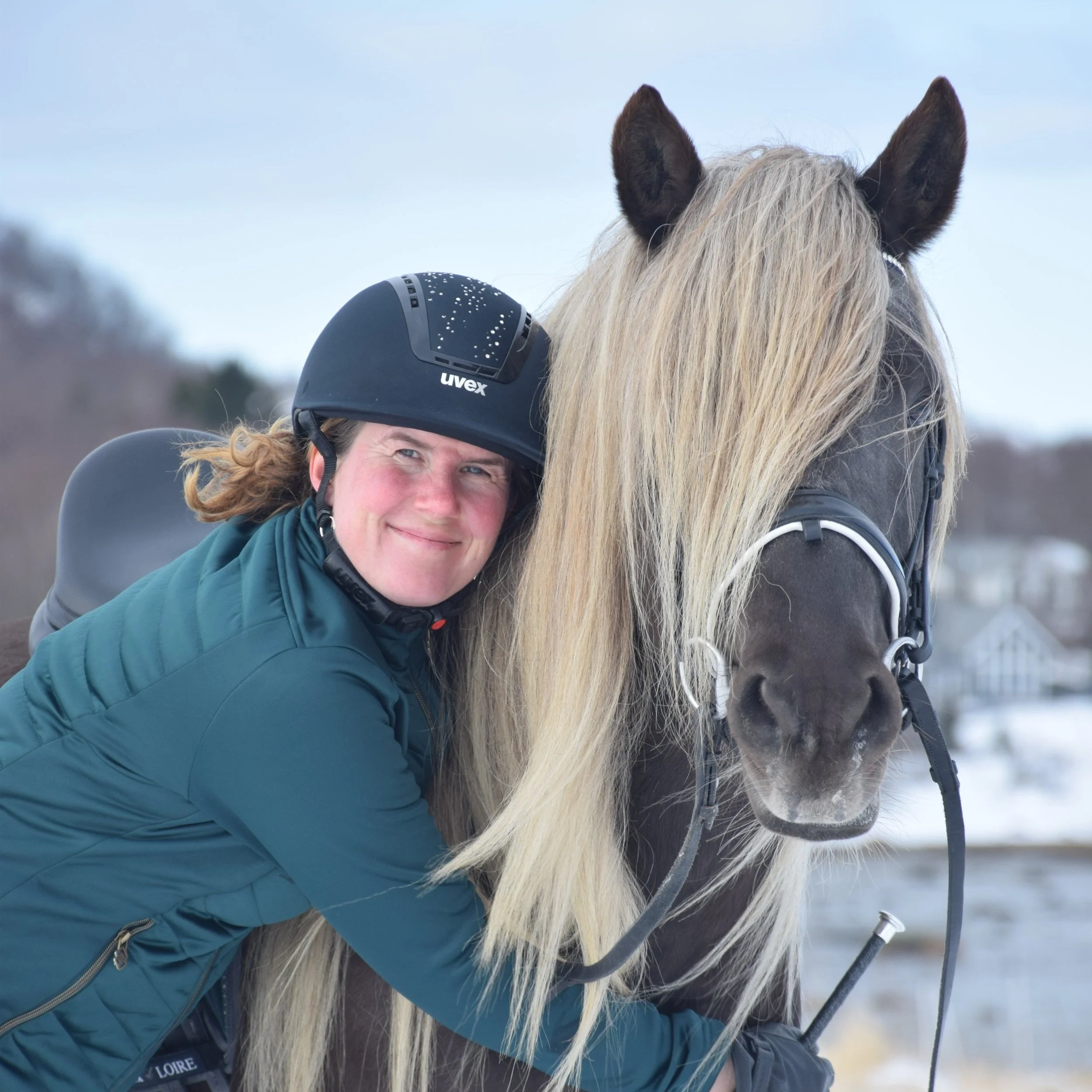 Nærbilde av en person som smiler,  inntil en brun hest med blond man