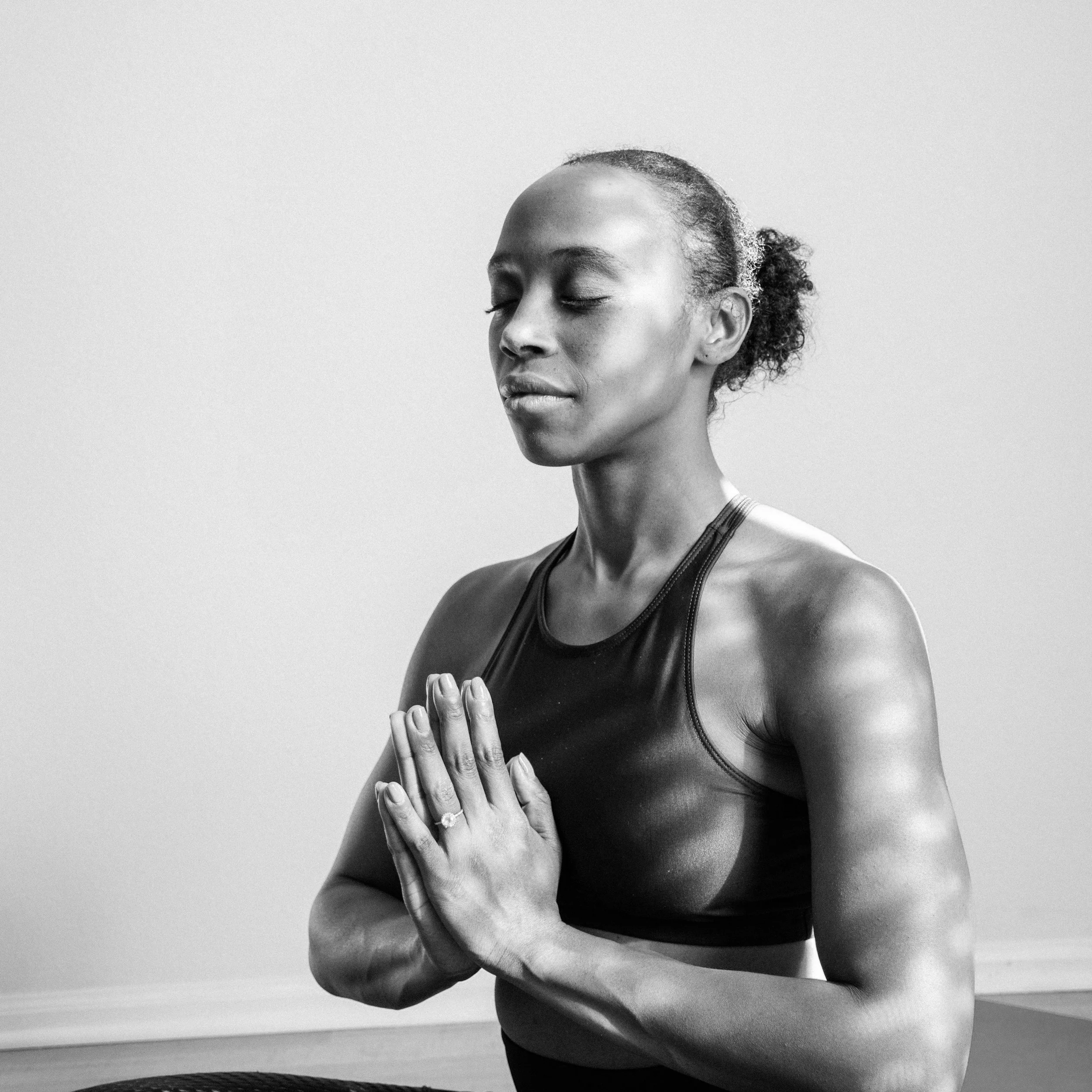 Woman practicing yoga with hands in prayer position, eyes closed, wearing sportswear, in a peaceful setting.