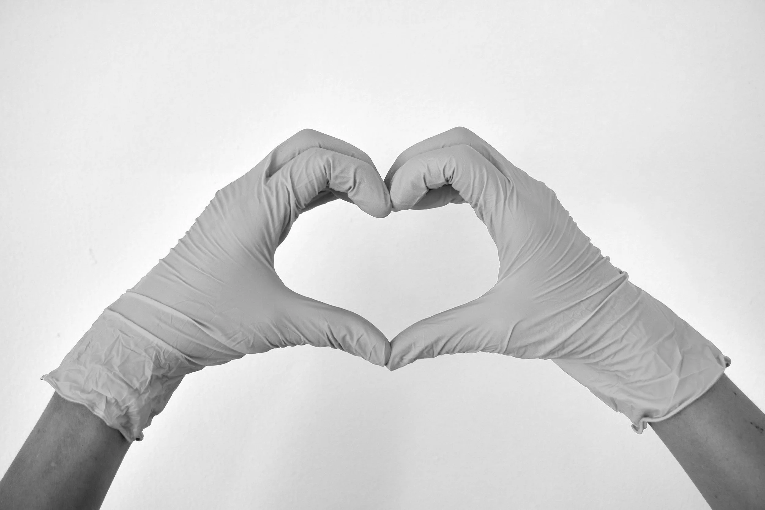 Hands wearing gloves forming a heart shape on a light background.