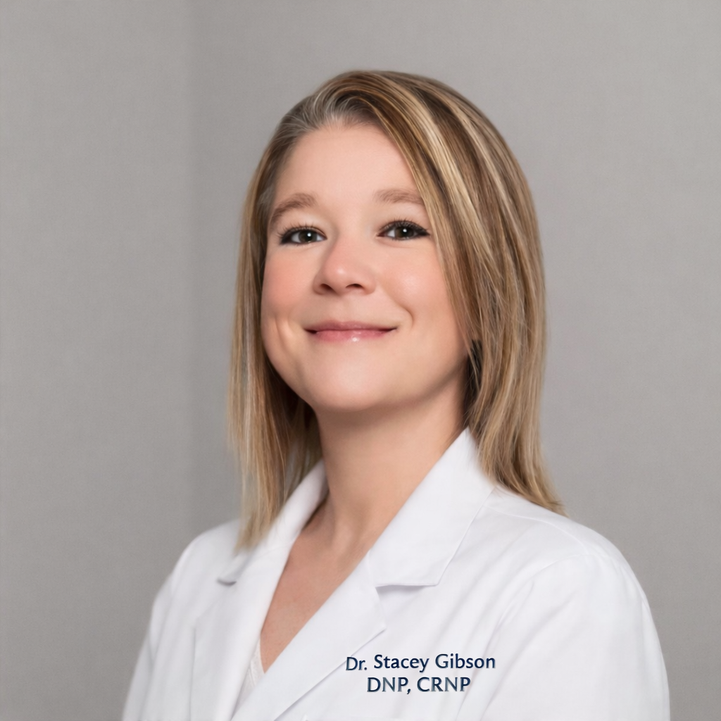 Portrait of Dr. Stacey Gibson, a healthcare professional, wearing a white lab coat with her name and credentials embroidered on it, smiling against a plain background.