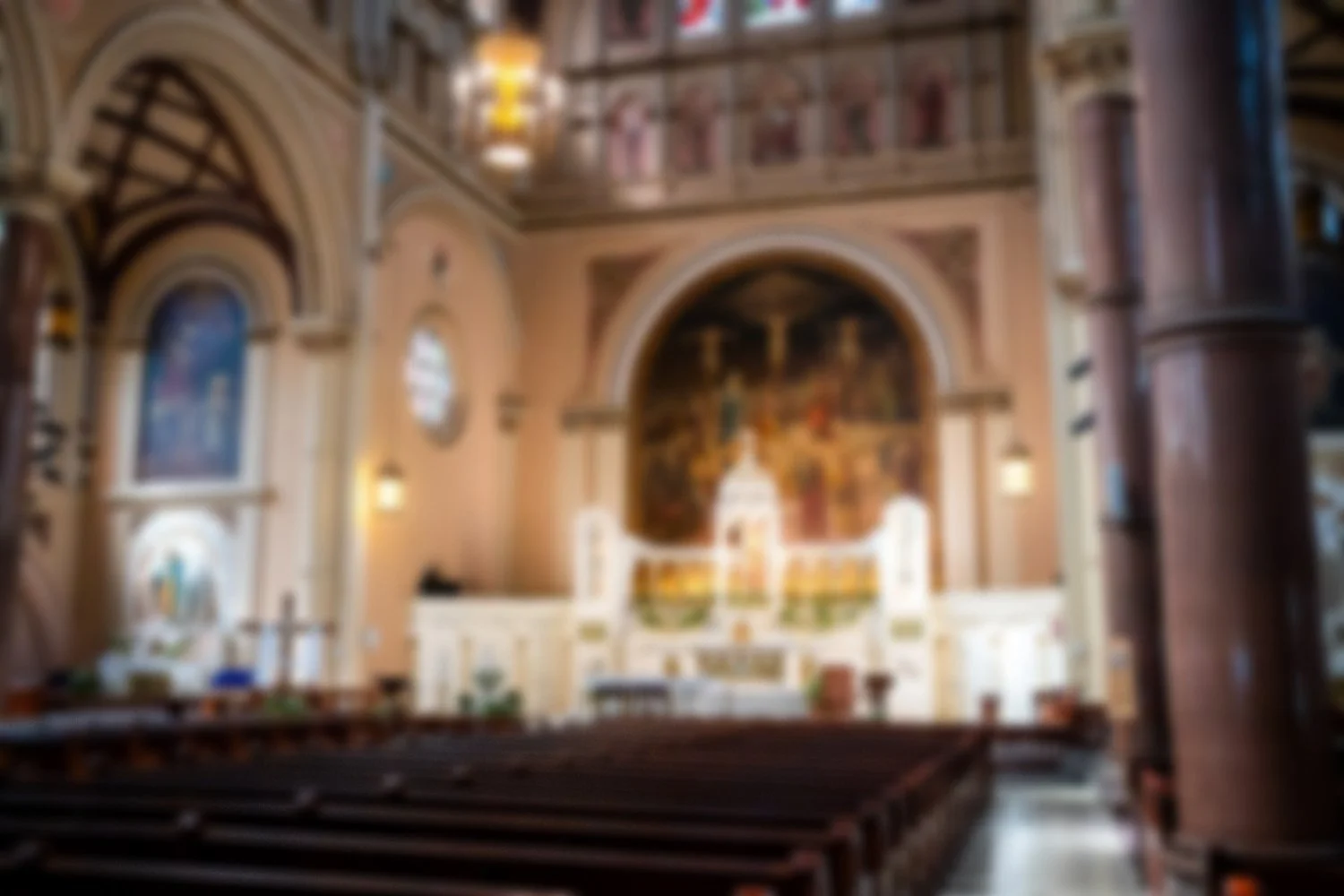 Blurred interior of a church with an altar, religious paintings, and wooden pews.