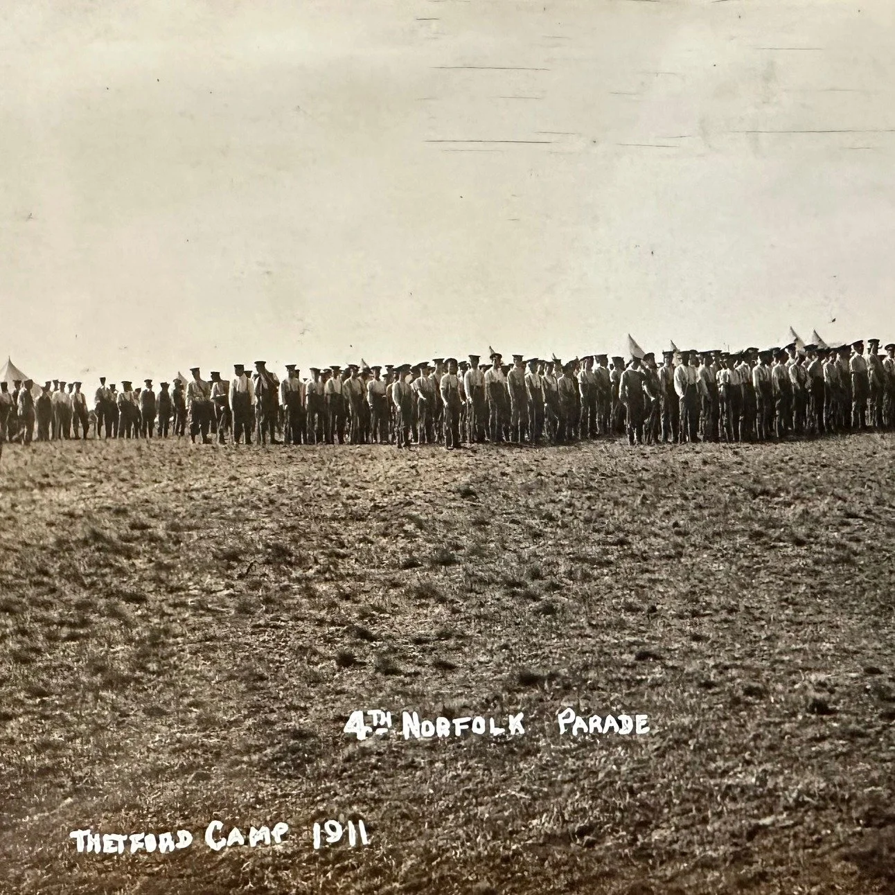 A photograph postcard showing the 4th Norfolk, Parade, Thetford Camp 1911. The postcard is sent to Miss Jolly, Girton Villa, Victoria Park, New Chesterton, Cambridge. The sender writes:&lsquo;Thetford Camp Friday
Dear Frances, Please send fourwheels 