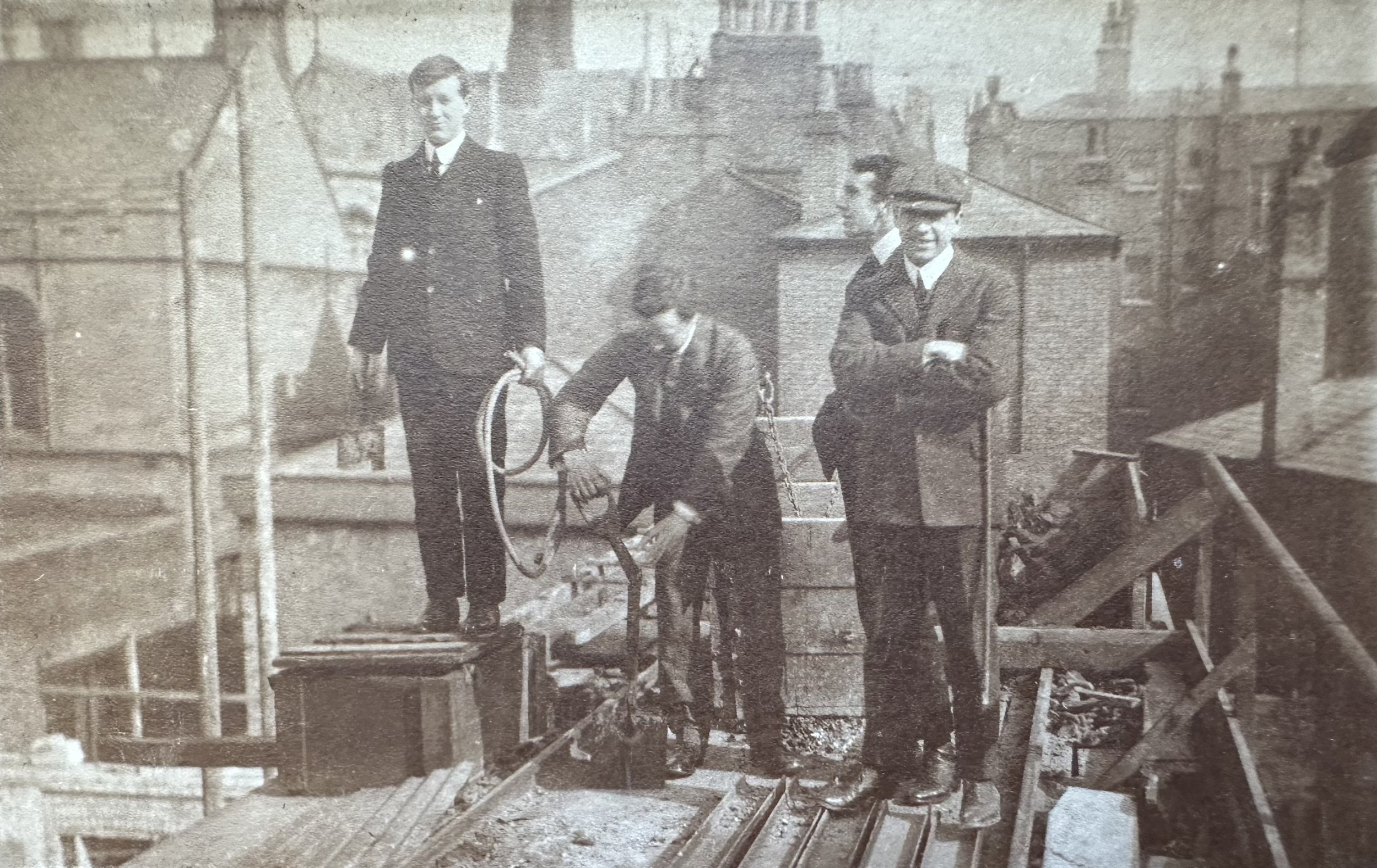 Four men on a rooftop during building works (Cambridge, probable). MBHPC-018
