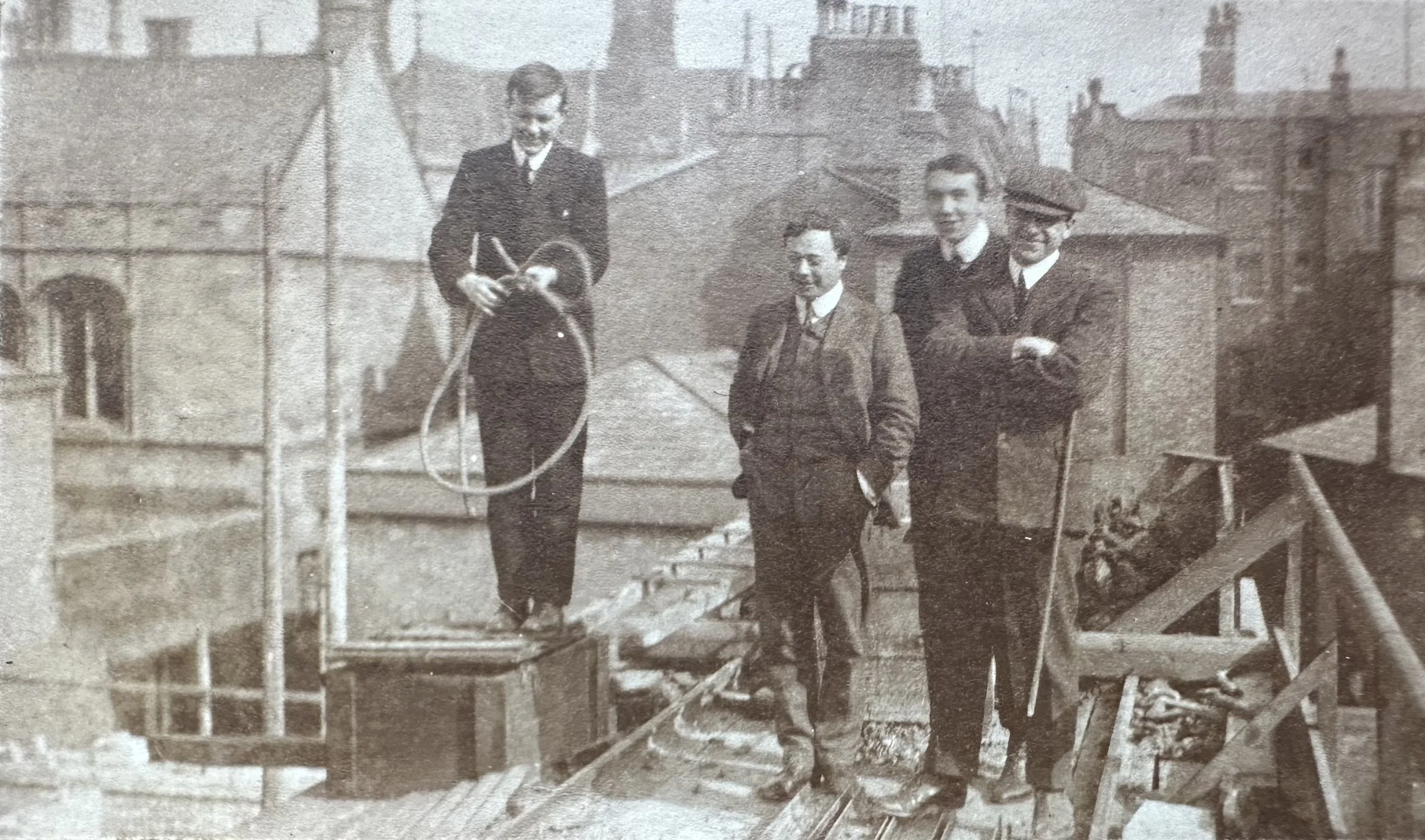 Four men on a rooftop during building works (Cambridge, probable). MBHPC-019