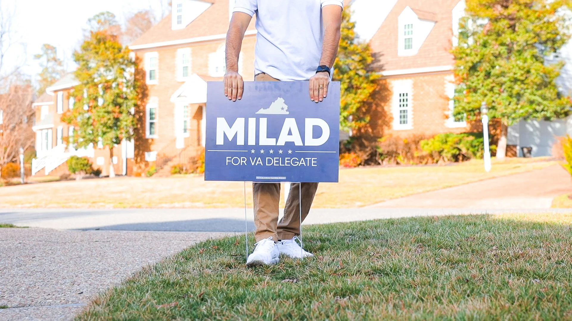 Person standing on grass holding a sign that reads "Milad for VA Delegate."